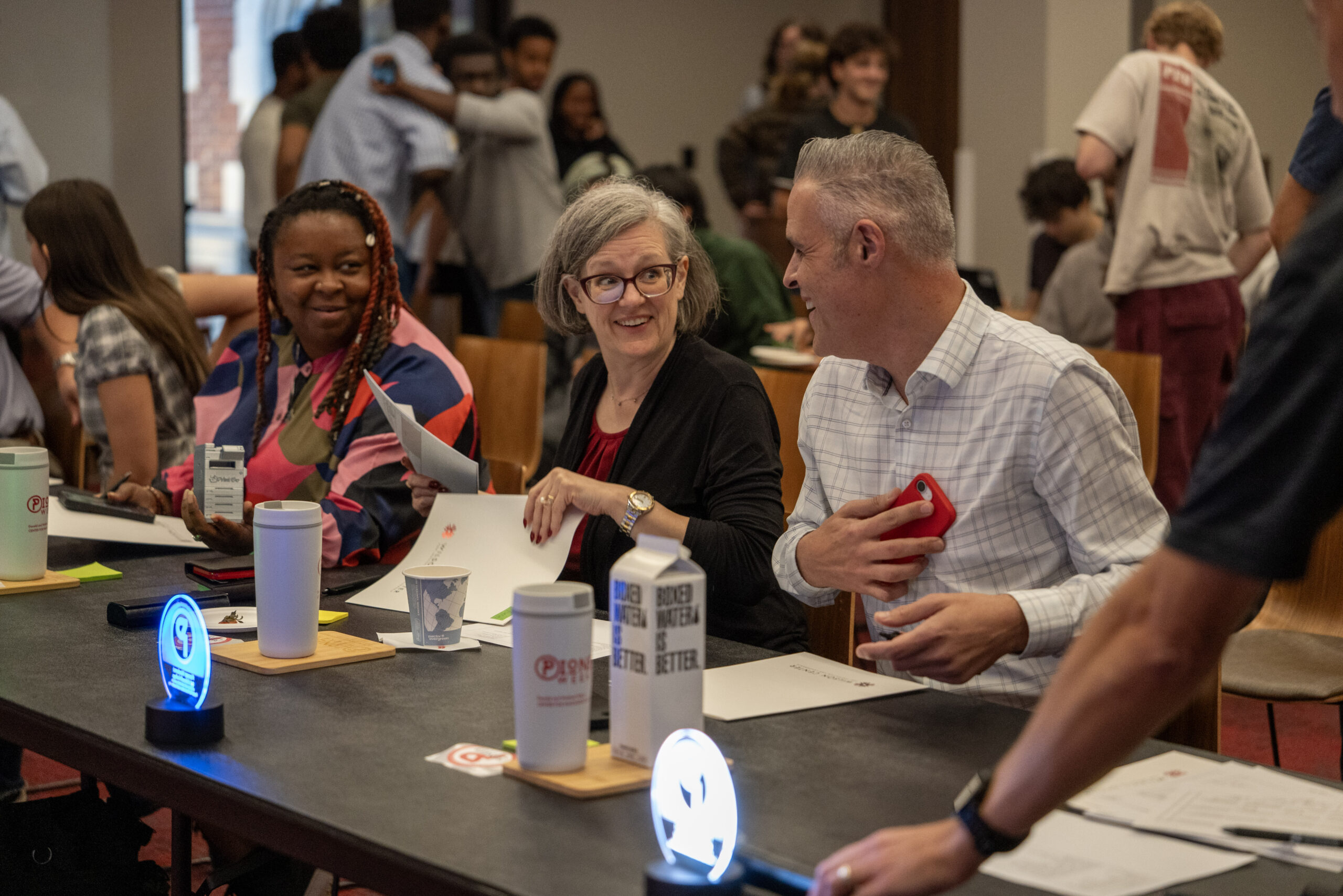 Three judges share a laugh after the final presentation of the event, while students rise from their seats in the audience and congratulate each other for a job well done.